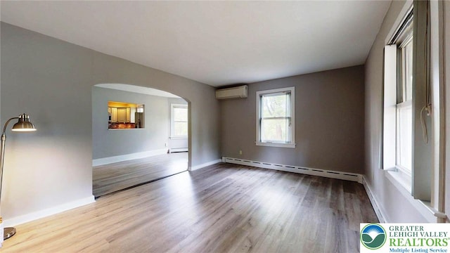 spare room featuring wood finished floors, arched walkways, a baseboard radiator, and a wall unit AC