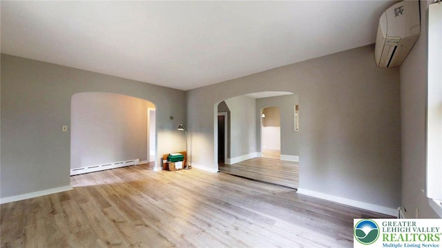 empty room with a wall unit AC, arched walkways, wood finished floors, baseboards, and a baseboard radiator