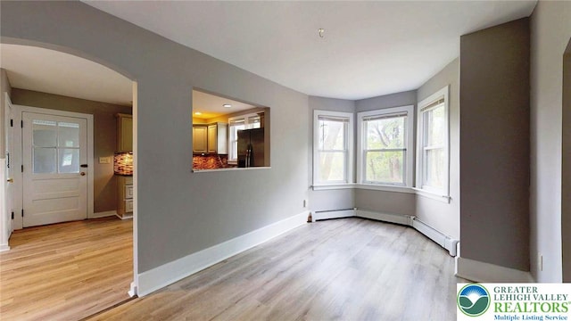 interior space featuring light wood-type flooring, arched walkways, and baseboards