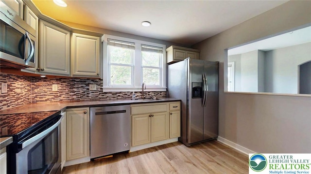 kitchen with dark countertops, light wood-type flooring, cream cabinetry, backsplash, and stainless steel appliances
