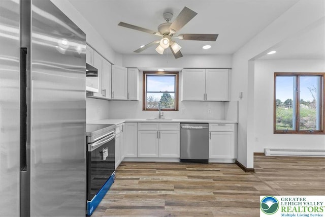kitchen with white cabinets, appliances with stainless steel finishes, a sink, light countertops, and a baseboard radiator