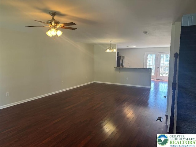 unfurnished living room featuring baseboards, ceiling fan with notable chandelier, and dark wood-style floors