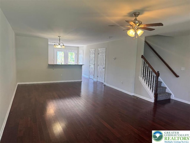 unfurnished living room featuring dark wood-type flooring, stairs, ceiling fan with notable chandelier, and baseboards