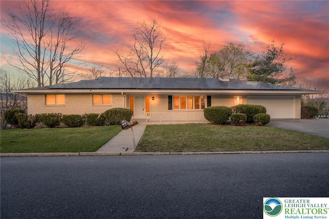 view of front facade featuring driveway, a lawn, a garage, brick siding, and roof mounted solar panels