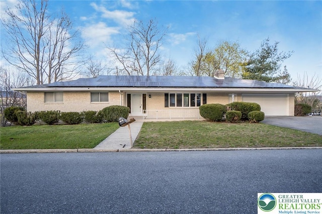 single story home with brick siding, a garage, a front yard, roof mounted solar panels, and driveway