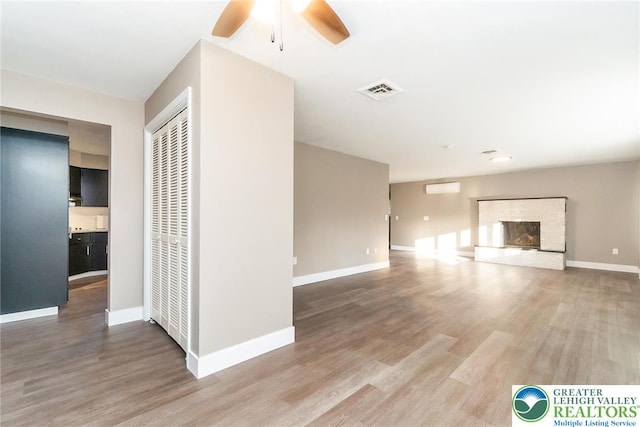unfurnished living room with ceiling fan, a brick fireplace, wood finished floors, and visible vents