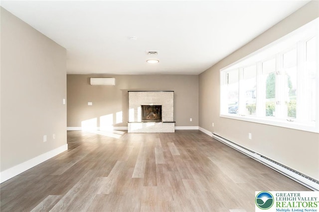 unfurnished living room with visible vents, wood finished floors, baseboards, a baseboard radiator, and a fireplace with raised hearth