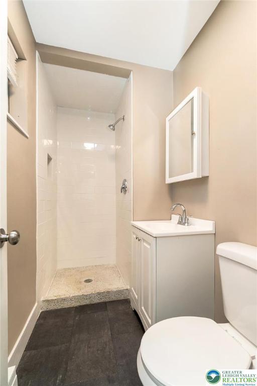 bathroom featuring vanity, a tile shower, and toilet
