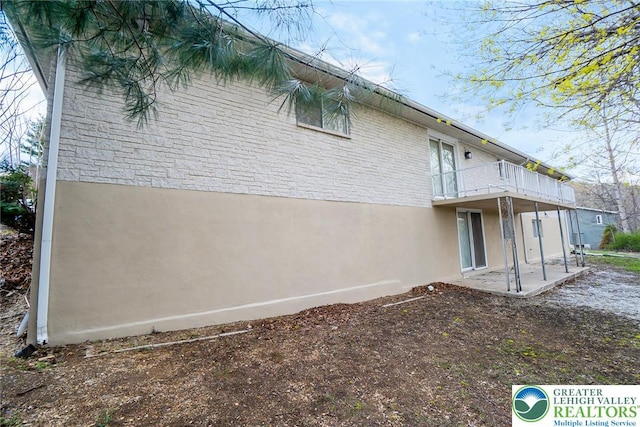 back of house featuring stucco siding, a patio area, brick siding, and a balcony