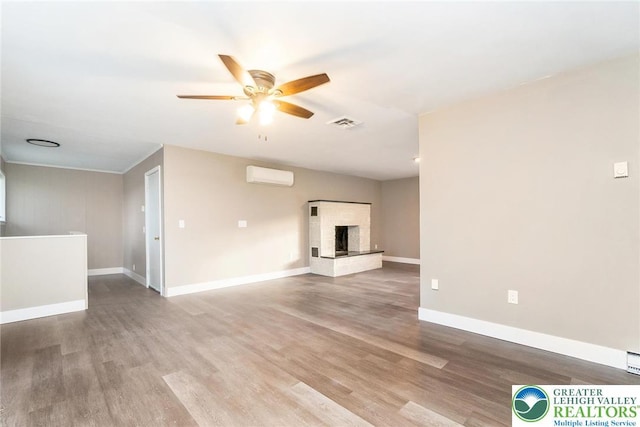 unfurnished living room with visible vents, a brick fireplace, wood finished floors, baseboards, and a ceiling fan