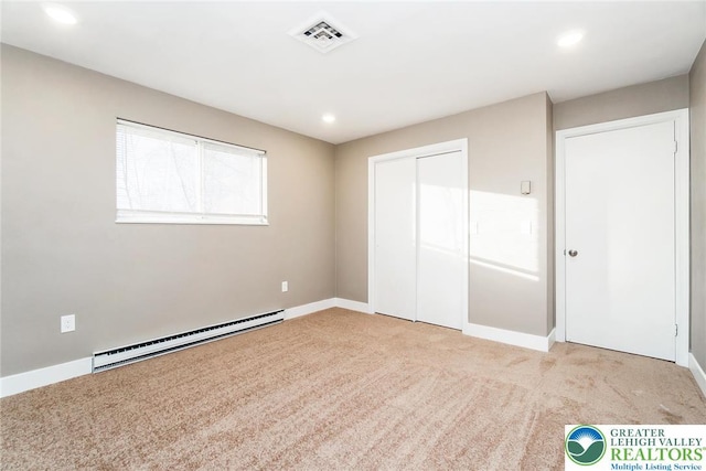 unfurnished bedroom with light colored carpet, a baseboard heating unit, visible vents, and a closet
