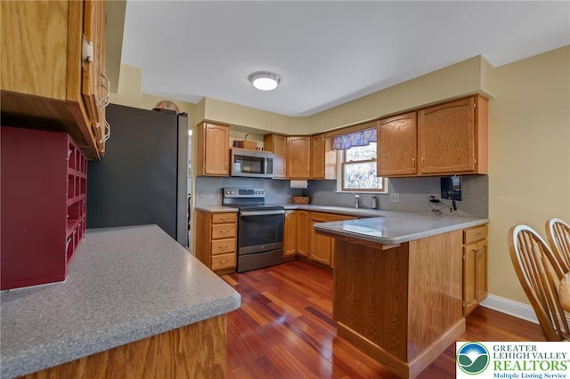 kitchen featuring decorative backsplash, a peninsula, dark wood-style floors, a sink, and stainless steel appliances
