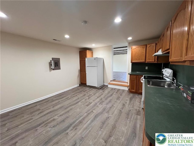 kitchen featuring brown cabinetry, freestanding refrigerator, light wood finished floors, under cabinet range hood, and recessed lighting