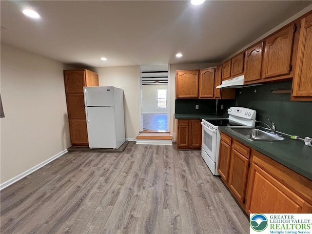 kitchen with brown cabinets, dark countertops, a sink, light wood-style floors, and white appliances