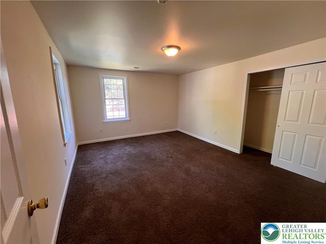 unfurnished bedroom with dark carpet, baseboards, and a closet