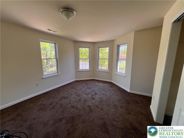 empty room with visible vents, baseboards, plenty of natural light, and dark colored carpet