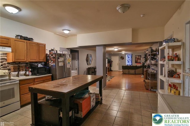 kitchen with freestanding refrigerator, under cabinet range hood, light tile patterned flooring, and electric stove