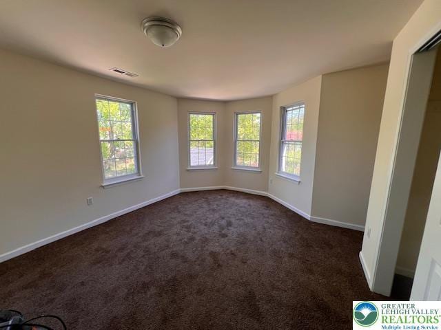spare room featuring baseboards, dark colored carpet, and visible vents
