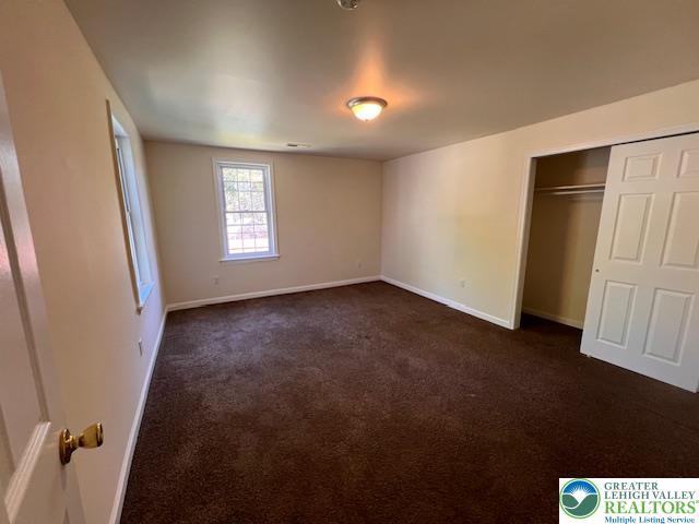 unfurnished bedroom featuring baseboards, a closet, and dark carpet