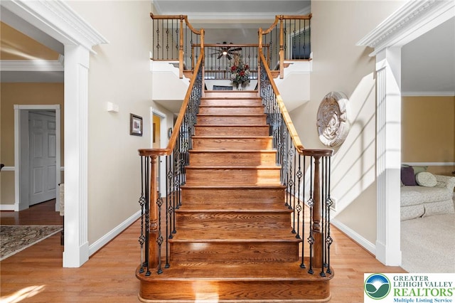 stairs featuring crown molding, baseboards, a high ceiling, and wood finished floors