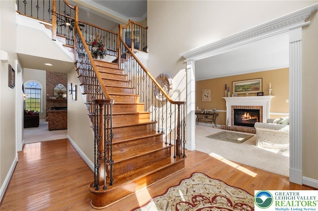 staircase with a brick fireplace, wood finished floors, and a towering ceiling