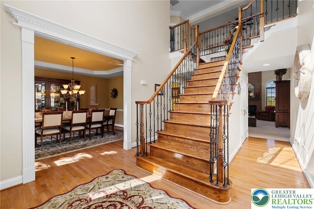 stairs featuring a towering ceiling, wood finished floors, baseboards, a chandelier, and ornamental molding