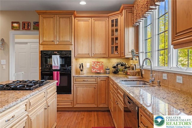 kitchen featuring a sink, light wood-style floors, decorative backsplash, glass insert cabinets, and black appliances