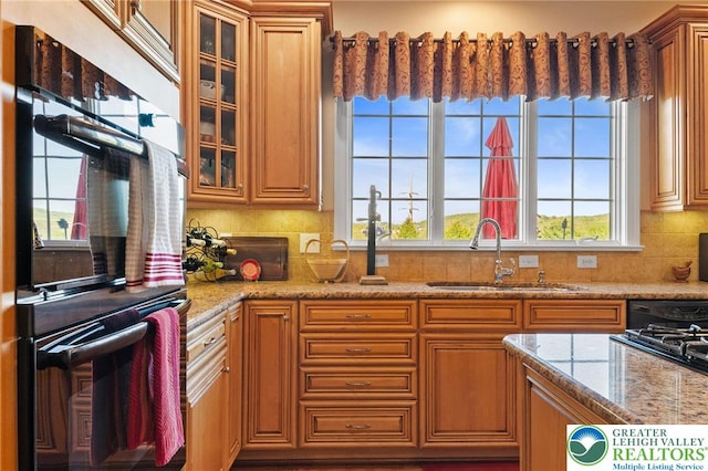 kitchen featuring plenty of natural light, tasteful backsplash, a sink, light stone counters, and double oven