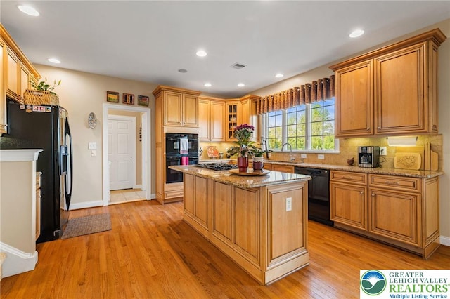 kitchen featuring light stone countertops, a center island, black appliances, and tasteful backsplash