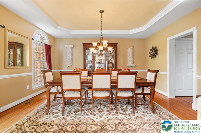 dining space with light wood-style floors, baseboards, a tray ceiling, and a chandelier