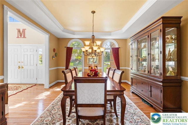 dining space featuring ornamental molding, baseboards, light wood-type flooring, a tray ceiling, and a notable chandelier