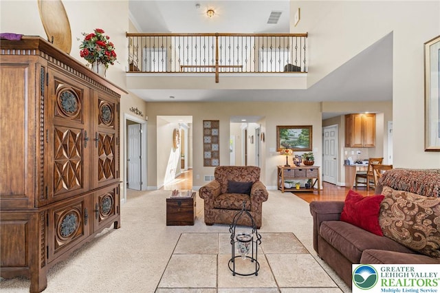 living room featuring light colored carpet, baseboards, visible vents, and a towering ceiling