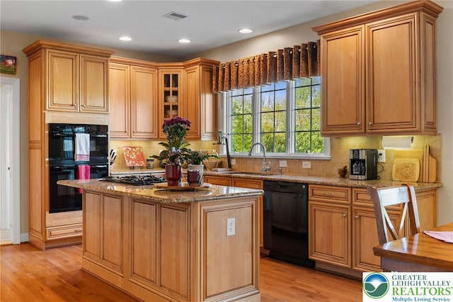 kitchen with light stone countertops, a center island, a sink, light wood-style flooring, and black appliances