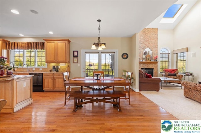 dining room with light wood-type flooring, a brick fireplace, a notable chandelier, and a healthy amount of sunlight