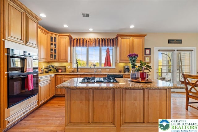 kitchen featuring gas cooktop, dobule oven black, visible vents, a center island, and light wood-style floors