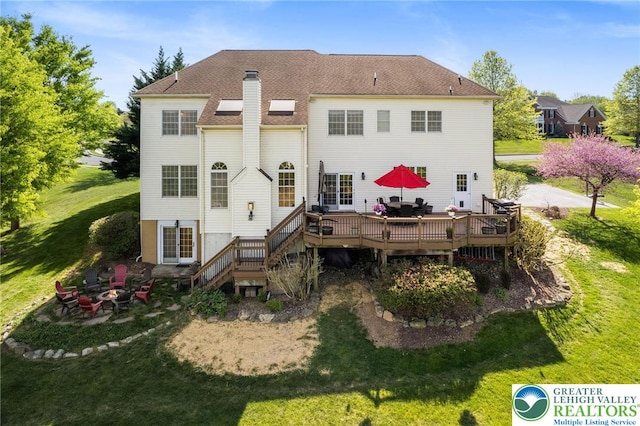 rear view of property with a shingled roof, a deck, a chimney, a lawn, and a fire pit