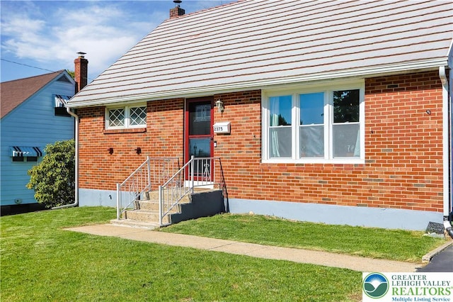 view of front facade featuring a chimney, a front yard, and brick siding