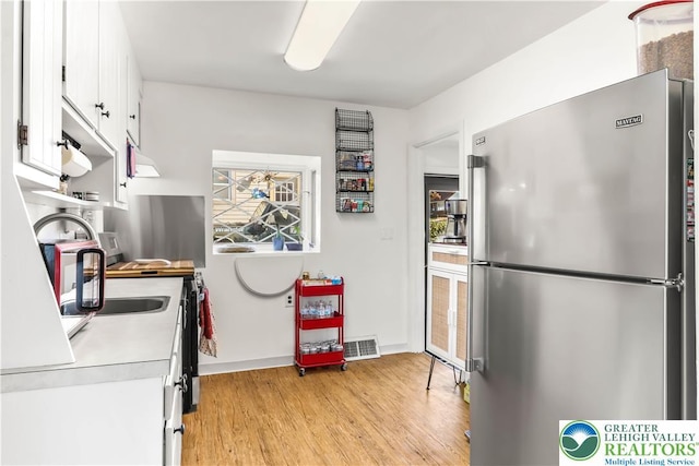 kitchen featuring visible vents, freestanding refrigerator, light wood-style floors, light countertops, and white cabinets