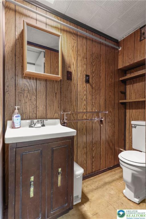 half bathroom with vanity, toilet, and wood walls