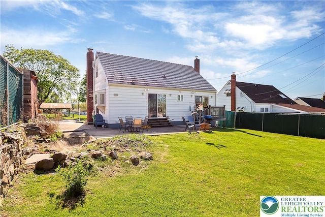 rear view of property featuring fence, a chimney, a patio area, entry steps, and a lawn