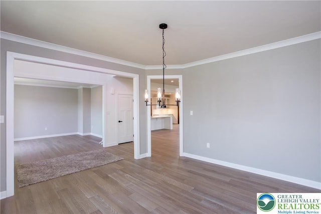 unfurnished dining area with crown molding, baseboards, wood finished floors, and a notable chandelier