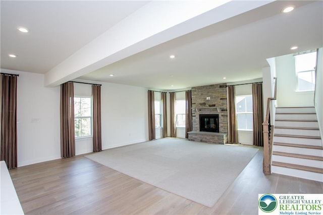 unfurnished living room with light wood-type flooring, baseboards, a fireplace, and stairway
