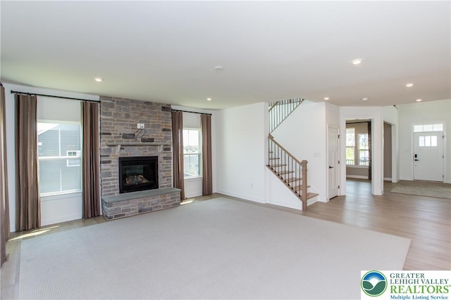 unfurnished living room featuring a large fireplace, wood finished floors, stairway, baseboards, and recessed lighting