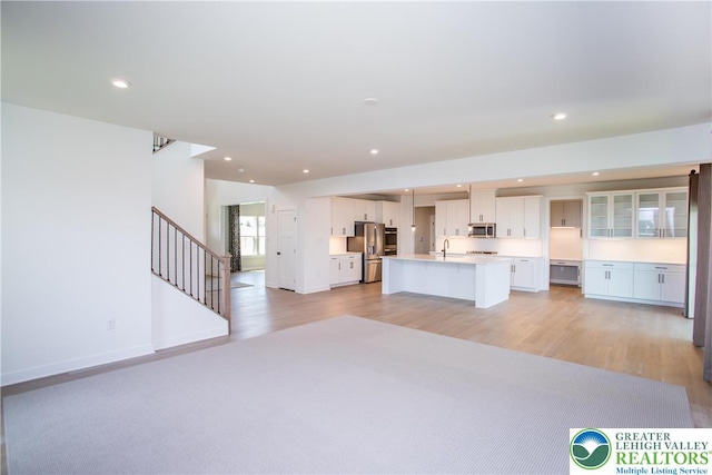 kitchen featuring appliances with stainless steel finishes, an island with sink, light wood finished floors, and open floor plan