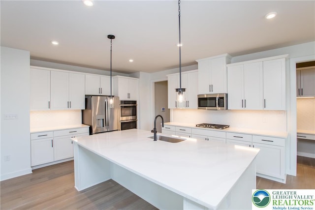 kitchen featuring light wood-style floors, a center island with sink, tasteful backsplash, a sink, and appliances with stainless steel finishes