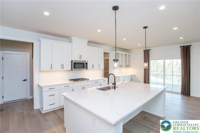 kitchen with appliances with stainless steel finishes, a center island with sink, a sink, light wood finished floors, and white cabinetry