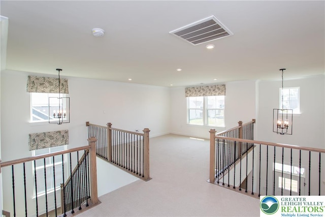 hall featuring carpet floors, visible vents, an upstairs landing, and a chandelier