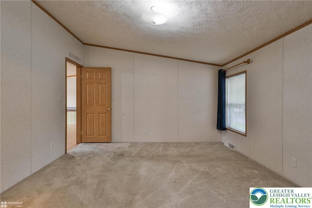 carpeted spare room with visible vents, ornamental molding, and a textured ceiling