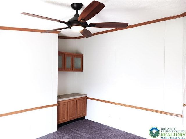 spare room with dark colored carpet, a ceiling fan, and ornamental molding