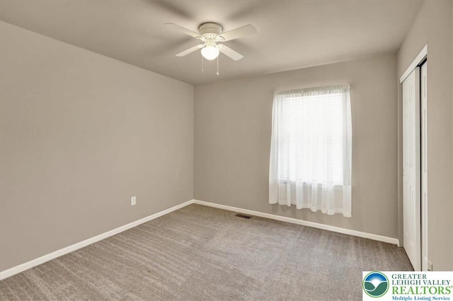 carpeted spare room with visible vents, a ceiling fan, and baseboards